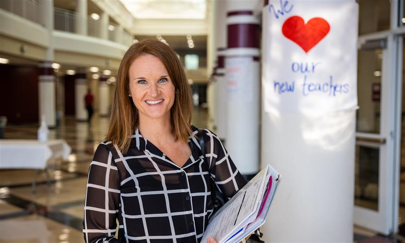 A woman holding a binder smiles while standing in front of a sign that reads \